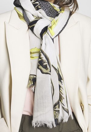 Valkoinen, musta ja keltainen kuvioitu huivi solmittuna kaulaan, puettuna beige bleiserin ja vaaleanpunaisen topin päälle.