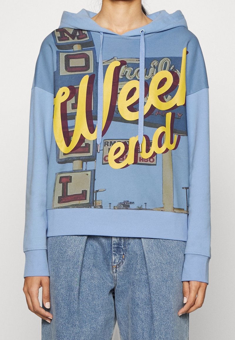 Jasnoniebieska bluza z kapturem z dużą żółtą i bordową grafiką z napisem "Weekend" oraz wzorem znaku motelu. Miękki materiał.