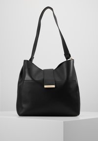 Czarna skórzana torebka o gładkiej fakturze, z pojedynczym paskiem na ramię i złotym elementem ozdobnym na przedniej klapce.