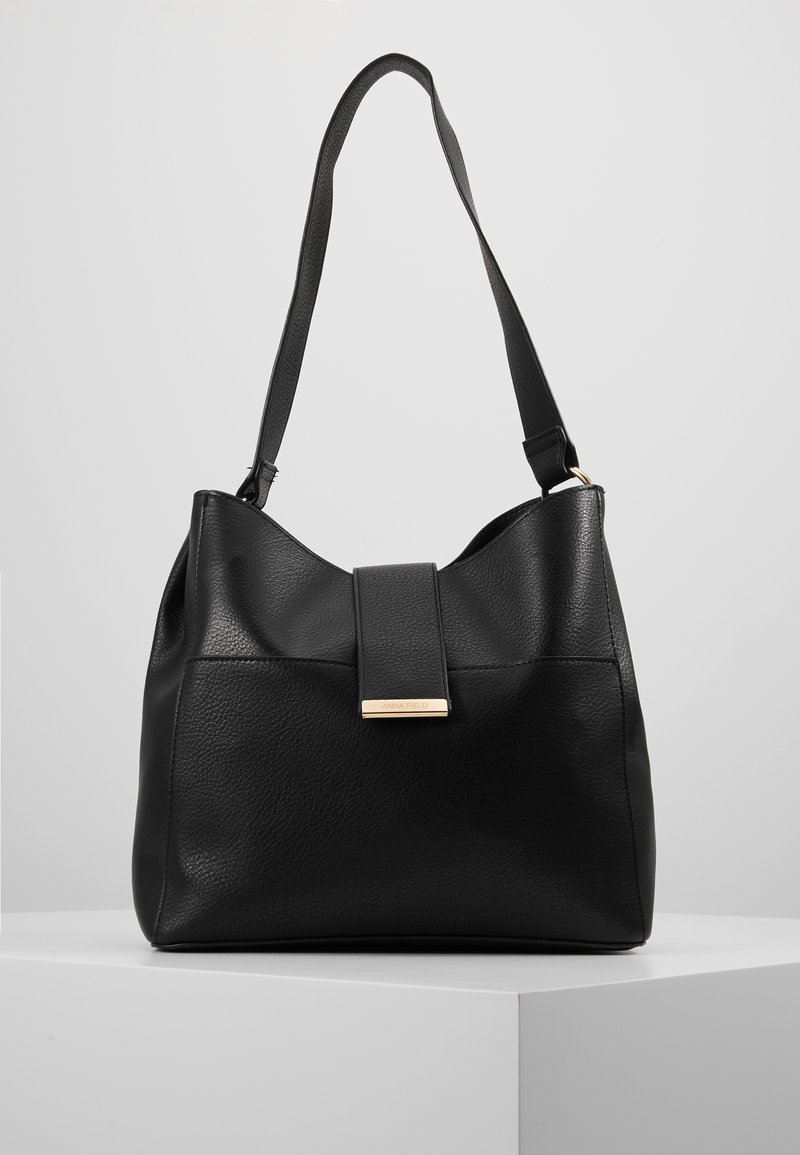 Czarna skórzana torebka o gładkiej fakturze, z pojedynczym paskiem na ramię i złotym elementem ozdobnym na przedniej klapce.