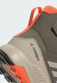 Πεζοπορικό παπούτσι Terrex με πράσινο επάνω μέρος, πορτοκαλί λεπτομέρειες, υφή υλικού, ενισχυμένη φτέρνα και ελαφρώς γκρι καουτσούκ σόλα με πρόσφυση.
