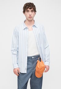Πουκάμισο με κουμπιά σε ανοιχτό μπλε και λευκές ρίγες, βαμβακερό υλικό, άνετη εφαρμογή, συνδυασμένο με γκρι τζιν παντελόνι και πορτοκαλί καπέλο προσαρτημένο.