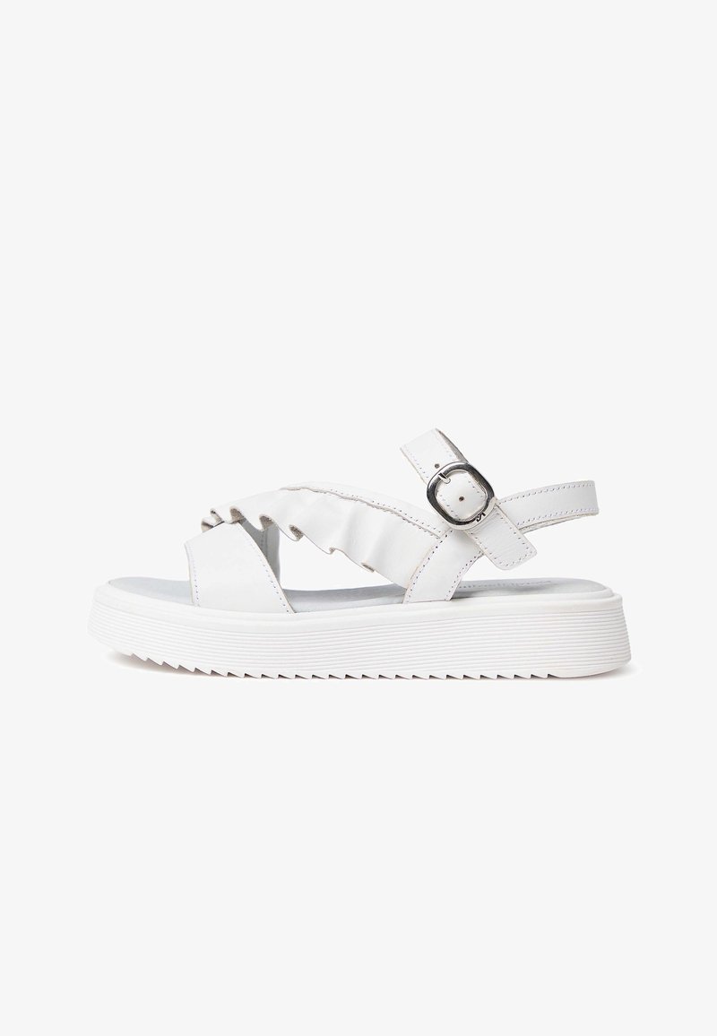 Sandale blanche avec semelle épaisse à rainures, bride cheville ajustable avec boucle en métal, et détail de bride avant à volants.