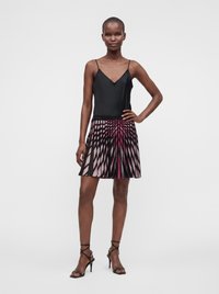 Femme portant un haut sans manches noir, une jupe noire et rose à motifs et des sandales noires à talons hauts avec des lanières, debout, une main sur la hanche.