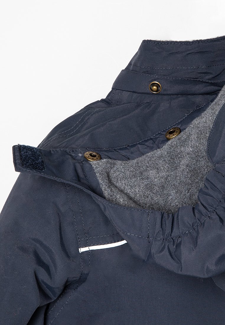 Giacca blu navy con un morbido rivestimento in pile grigio, caratterizzata da bottoni a pressione dorati e un colletto parzialmente zip. Include dettagli elasticizzati per una vestibilità ottimale.