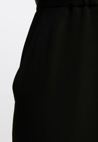 Black fabric with a smooth texture, featuring a side pocket and elastic waistband, emphasizing a simple and functional design.