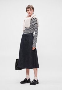 Μαύρη τζιν φούστα σε Α γραμμή με ζώνη, συνδυασμένη με μαύρο και λευκό ριγέ μακρυμάνικο τοπ, μπεζ σ scarf και μαύρα loafers.