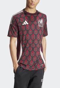 Camisa Adidas color burdeos con un diseño de patrón en forma de gota de color verde; presenta acentos en blanco y un logo de México. Mangas cortas y cuello redondo.