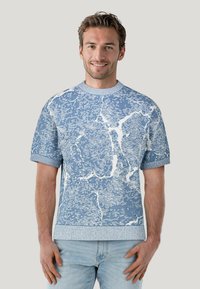Maglione a maniche corte color azzurro chiaro con un motivo astratto bianco. Texture a maglia e colletto e polsini a coste. Vestibilità casual e rilassata.