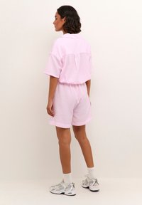 Chemise rose clair à manches courtes et shorts assortis à motif à carreaux. Coupe décontractée, détail col, associés à des chaussures de sport blanches et des chaussettes.