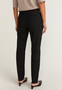 Musta muotopuvut, joissa on kapea istuvuus, takana tasapocketit ja tasainen tekstuuri. Yhdistetty matalakorkoisiin mustiin kenkiin.