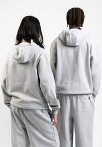 Grå hættetrøjer lavet af blødt stof med kengurulommer. Designet inkluderer en justerbarhætte og matchende grå sweatpants med sidelommer.