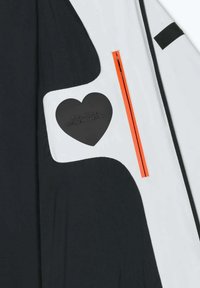 Interno di giacca bianco e nero con una cerniera arancione. Presenta un dettaglio a forma di cuore nero testurizzato con la scritta "Fatto con amore, progettato in Toscana."