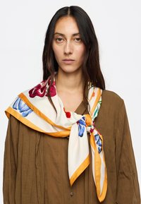 Pañuelo de seda con un patrón floral en tonos azul, rojo y verde, bordeado en naranja y anudado alrededor del cuello.