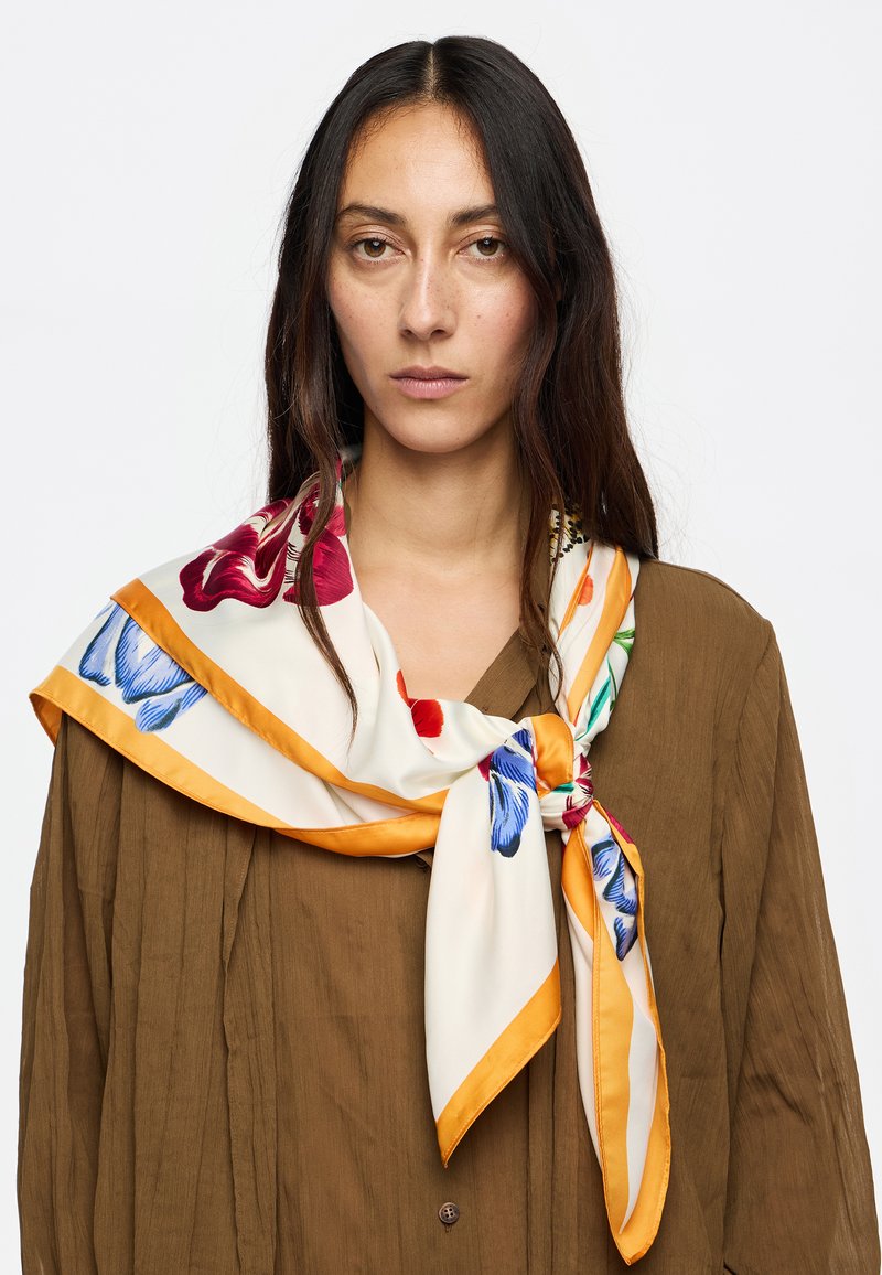 Pañuelo de seda con un patrón floral en tonos azul, rojo y verde, bordeado en naranja y anudado alrededor del cuello.