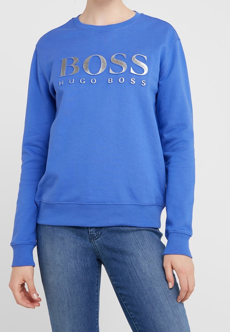 Niebieska bluza z okrągłym dekoltem, z srebrnym logo "BOSS HUGO BOSS" na piersi. Miękka tkanina oraz ściągacze przy mankietach i dolnym wykończeniu.