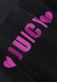 Μαύρο ύφασ�μα με απαλή υφή, με έντονα μωβ γράμματα που σχηματίζουν τη λέξη "JUICY" και ένα μικρό γραφικό καρδιάς.