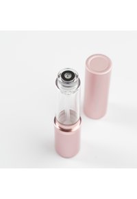 Przezroczysty szklany pojemnik z metaliczną, różowozłotą podstawą, wyposażony w wąski aplikator i dopasowaną nasadkę, o eleganckim, cylindrycznym kształcie.