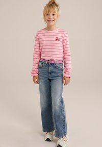 Růžová pruhovaná košile s dlouhým rukávem a výšivkou bruslí, doplněná volnými modrými džínami a bílými teniskami s barevnými akcenty.