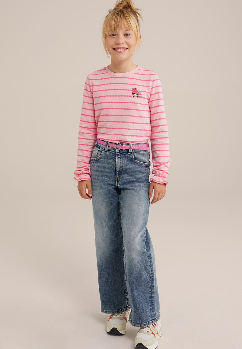 Růžová pruhovaná košile s dlouhým rukávem a výšivkou bruslí, doplněná volnými modrými džínami a bílými teniskami s barevnými akcenty.