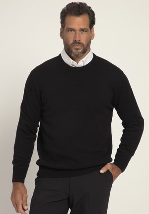Suéter negro de punto con cuello redondo, puños y dobladillo acanalados. Usado sobre una camisa blanca con cuello, expuesto sobre un fondo claro.