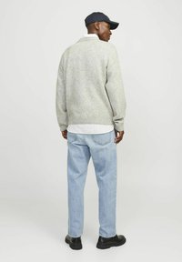 Suéter de punto gris claro con dobladillo acanalado, combinado con jeans de mezclilla azul claro. La persona lleva una gorra de béisbol azul marino y zapatos negros.