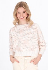 Strickpullover in Off-White mit pfirsichfarbigen Akzenten, ausgestattet mit einem gerippten Rundhalsausschnitt und langen Ärmeln, getragen über hellen Hosen.