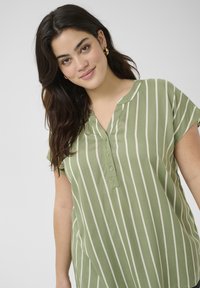 Chemise à rayures vertes en tissu léger, avec un col en V, des manches courtes et des détails de boutons, ornée de rayures verticales blanc cassé.