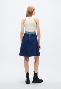 Φούστα α μπόυ με τζιν ύφασμα και πιο ανοιχτόγλυκη μπλε μέση, με φερμουάρ στο πίσω μέρος, συνδυασμένη με μια κρεμ ριπ μπλούζα χωρίς μανίκια και μαύρες μποτάκια αστραγάλου.