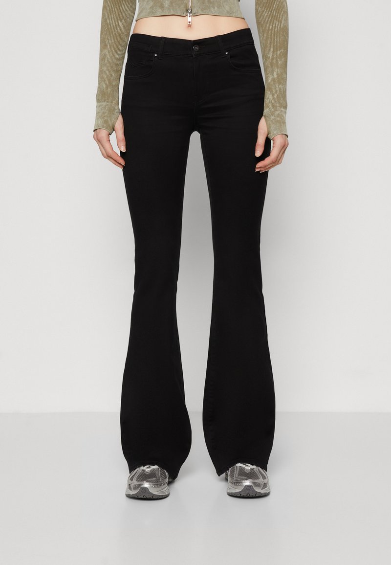 Sorte flagrende jeans med en glatt tekstur, midjehøyde, og fem lomme-design, kombinert med grå treningssko med netting og gummidetaljer.