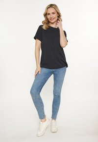 Sort kortærmet t-shirt parret med lyseblå skinny jeans og hvide sneakers, med en afslappet pasform og blød stofstruktur.