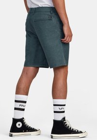 Mörkgröna shorts med rak skärning, med en bakficka, parat med svarta högskurna sneakers och vita randiga strumpor.