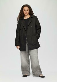 Schwarzer, doppelreihiger Trenchcoat mit Kragen, Fronttaschen und lockerer Passform, kombiniert mit grauen, weit geschnittenen Jeans und schwarzen Schuhen.