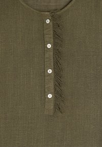 Oliwkowa lniana bluzka z okrągłym dekoltem, z rzędem białych guzików i frędzlami wzdłuż listwy.