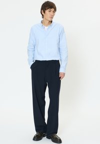 Jasnoniebieska koszula na guziki i granatowe plisowane spodnie, zestawione z błyszczącymi czarnymi butami. Koszula ma długie rękawy i klasyczny kołnierzyk.
