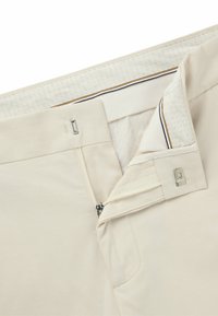 Pantaloni beige con zip sul davanti, chiusura a gancio e foderatura testurizzata. Le tasche esterne e un design pulito evidenziano la funzionalità.