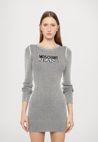 Šedé žebrované pletené šaty s dlouhými rukávy, s černým logem "MOSCHINO JEANS" přes hruď a těsným střihem, který zdůrazňuje siluetu.
