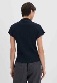 Haut tricoté côtelé marine avec des manches courtes et un col montant, présentant une coupe ajustée et une texture lisse. Porté avec un pantalon gris texturé.