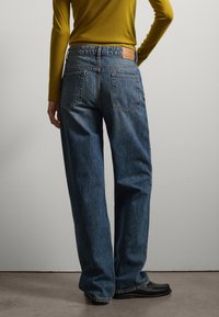 Jeans de mezclilla con un ajuste holgado, lavado azul medio, diseño de cinco bolsillos y una etiqueta de cuero en la parte trasera de la cintura. Frontales planos y piernas rectas.