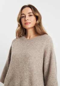 Beige oversized sweater gemaakt van zacht, fluffy materiaal met een ronde halslijn en verlaagde schouders, met een gestructureerde afwerking.