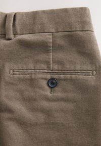 Pantalons en tissu marron à texture lisse, dotés d'une poche arrière, d'une fermeture à bouton et de détails de couture subtils.