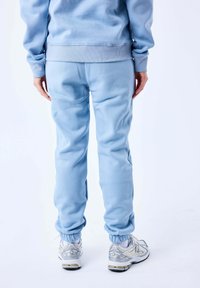 Lichtblauwe sweatpants van zachte stof, met ribgebreide boorden bij de enkels. Gecombineerd met wit en zilver gekleurde sportschoenen.