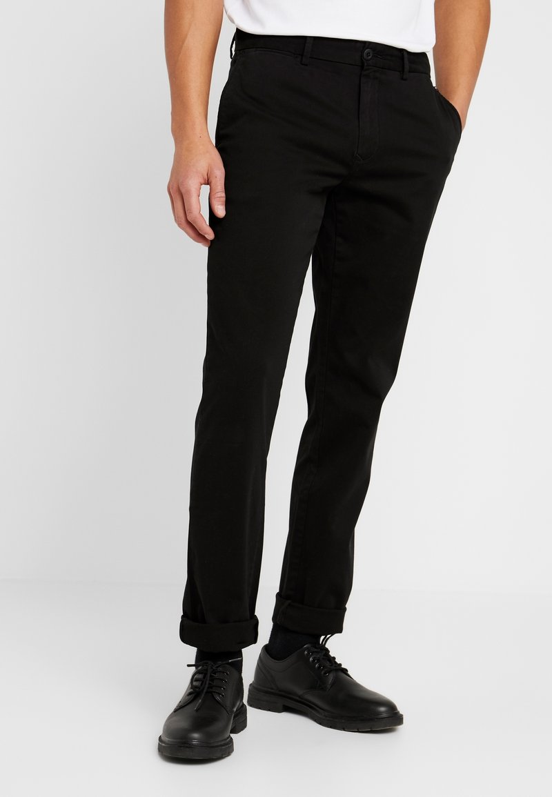 Černé chinos kalhoty z bavlny, se slim fit střihem, bočními kapsami a ohrnutými lemy. V kombinaci s černými šněrovacími botami.