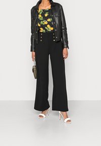 Svart läderjacka, blommig topp med gula citroner, högmidjade svarta byxor med guldfärgade knappar, och vita klacksandaler.