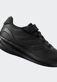 Baskets de sport noires avec un dessus texturé, bout renforcé, sangle ajustable et accents de logo marquants. Design élégant et léger.