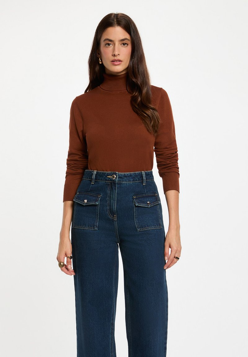 Haut col roulé marron à manches longues associé à un jean taille haute à jambes larges bleu foncé avec deux poches avant et des accents en métal.