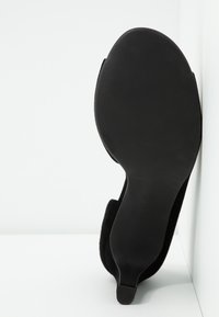 Chaussure à talon haut en suède noir avec une semelle lisse et courbée, dotée d'un bout pointu et d'un design minimaliste.