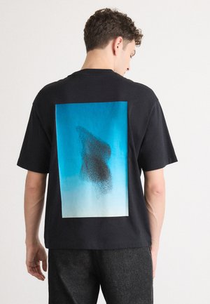 Black cotton t-shirt featuring a large blue gradient graphic on the back, depicting abstract black shapes. Short sleeves, relaxed fit.