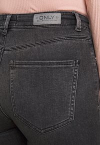 Pantalones vaqueros de mezclilla negra con una textura sutil, que presentan un bolsillo trasero y una etiqueta gris con la inscripción "ONLY" cosida en la cintura.