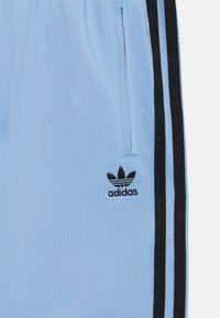 Lyseblå sportsshorts med sorte aksentstriper. Funksjoner inkluderer en elastisk midje og en liten svart adidas-logo nederst til venstre.